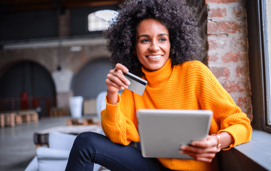 Woman in orange sweater holding a credit card and tablet